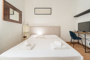 Ein Hotelzimmer mit Bett, Schreibtisch, Sessel, Fernseher, Spiegel und einem gerahmten Bild an der Wand.