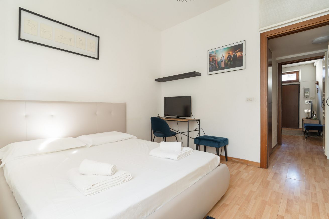 A hotel room with a large bed, a desk with a TV, and a chair.