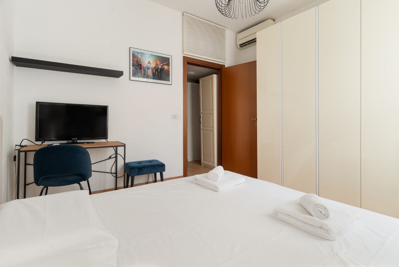Ein Hotelzimmer mit Bett, Schreibtisch mit Fernseher, Stuhl, Kleiderschrank und einer Tür zu einem weiteren Raum.