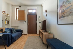 Ein kompakter Wohnraum mit einer Couch, einem Schreibtisch, einem Sessel, einer Heizung, einer Tür und einem gerahmten Bild an der Wand.