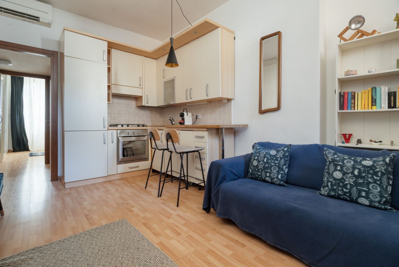 A modern kitchen with white cabinets, a dining area with a blue sofa, and a bookshelf.