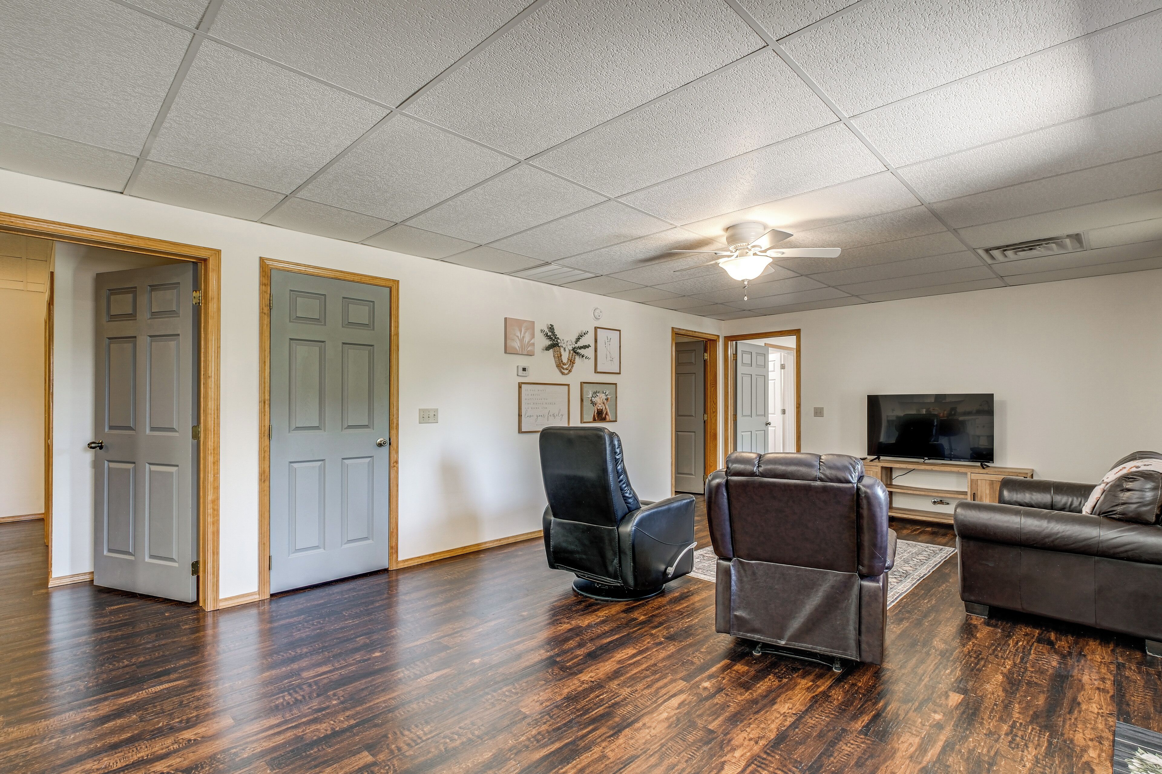 A spacious living room with hardwood flooring, a ceiling fan, and a flat-screen TV.
