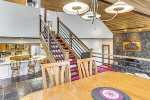 Eine geräumige Küche mit einer Holztreppe, einem Essbereich mit einem Holztisch und einer Steinwand mit Kamin.