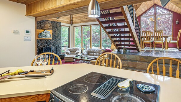 A kitchen with a stove, dining table, chairs, and a view of the outdoors through large windows. - Fire Pit & Wildlife Views! Tranquil Bend Retreat (Bend)