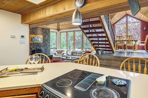 Une cuisine équipée d’une cuisinière, d’une table à manger, de chaises et offrant une vue sur l’extérieur grâce à de grandes fenêtres.