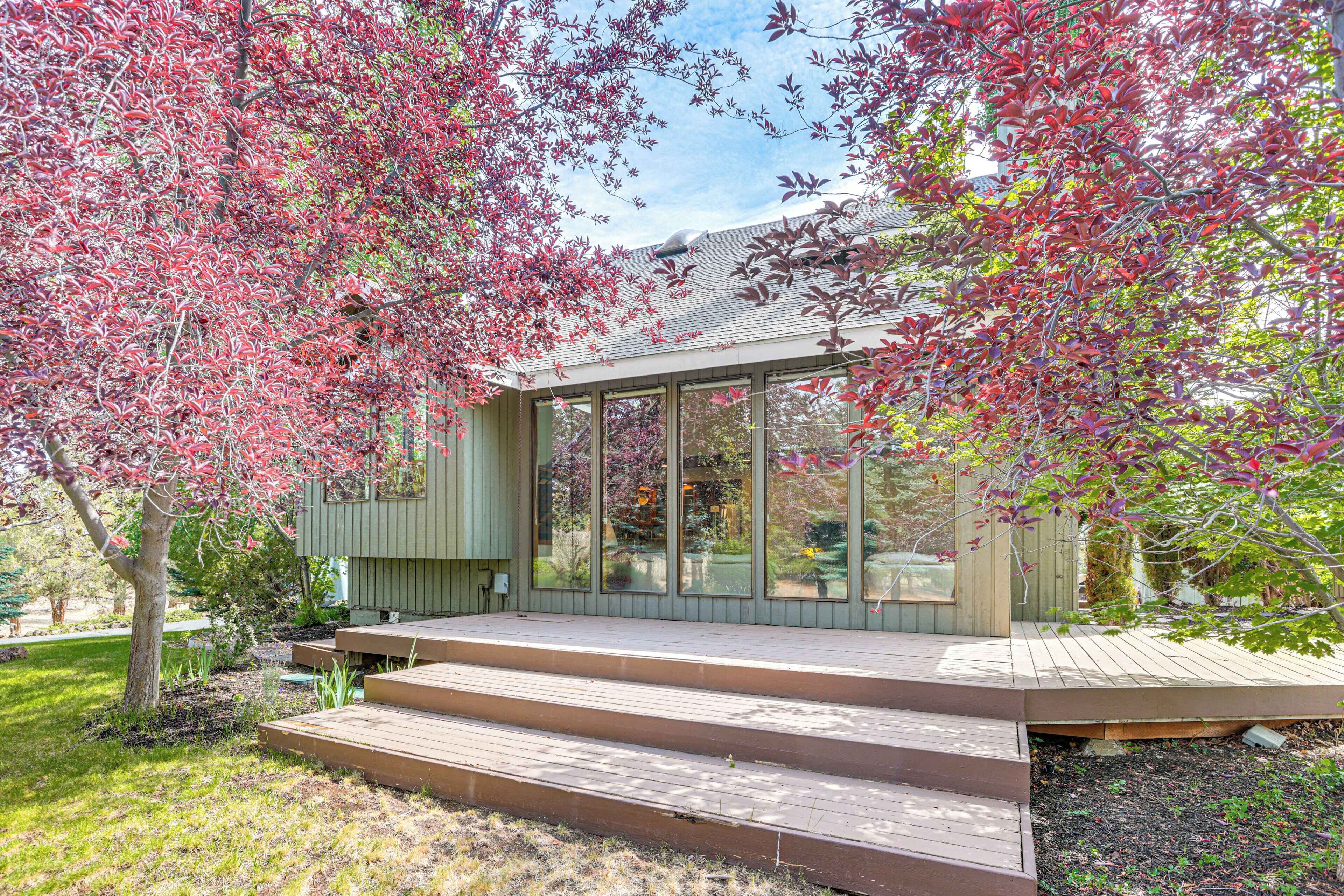 Une maison moderne avec une façade en verre, une terrasse en bois et un jardin agrémenté d’arbres aux feuilles rouges.