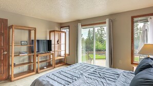 A bedroom with a large bed, a wooden TV stand, and a sliding glass door leading to a deck. - Fire Pit & Wildlife Views! Tranquil Bend Retreat (Bend)
