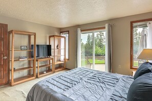 A bedroom with a large bed, a wooden TV stand, and a sliding glass door leading to a deck. - Fire Pit & Wildlife Views! Tranquil Bend Retreat (Bend)
