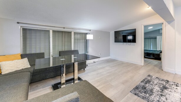 Ein modernes Wohnzimmer mit einem Esstisch mit Glasplatte, einem grauen Sofa und einem grauen Teppich.