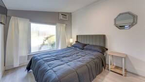 Ein Schlafzimmer mit einem Bett, einem Nachttisch, einem Spiegel und einem Fenster mit Vorhängen.