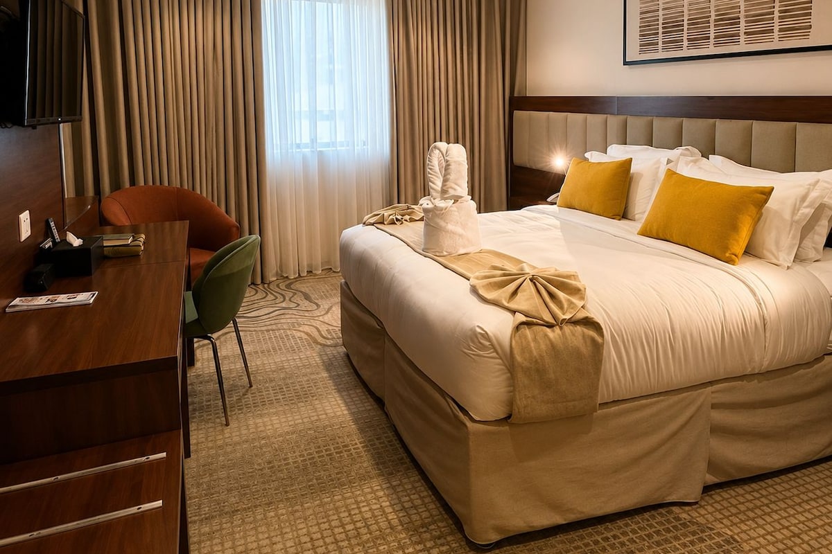 Habitación de hotel con una cama grande, un escritorio con silla, un televisor y una ventana con cortinas.