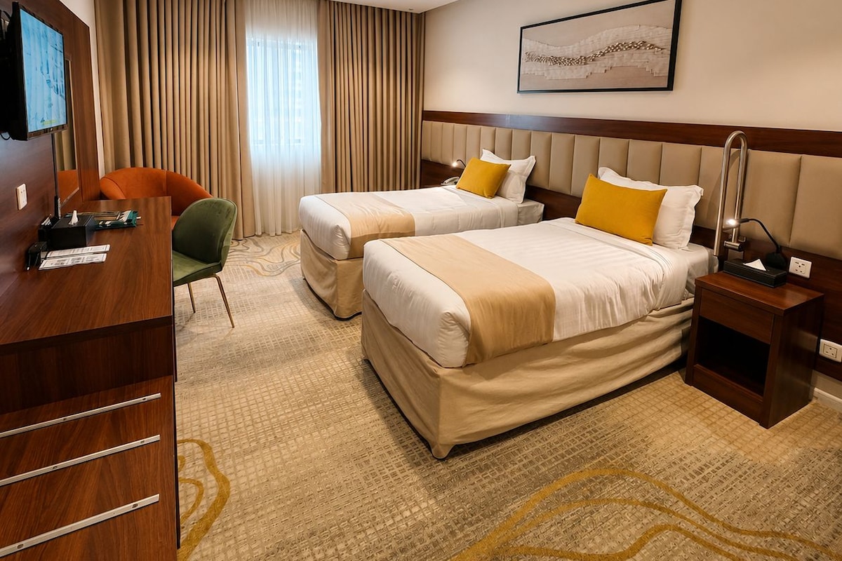 A hotel room with two beds, a desk, a chair, a television, and a painting on the wall.