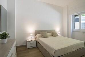 A bedroom with a bed, bedside tables, a nightstand, a lamp, a potted plant, and a window. - GuestHost - Cozy Apartment with Balcony (Como)