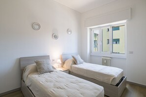 A bedroom with two beds, a window, and a radiator. - GuestHost - Cozy Apartment with Balcony (Como)