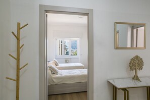 Ein Schlafzimmer mit Bett, Fenster, Kleiderhaken, Spiegel und einem kleinen Tisch.