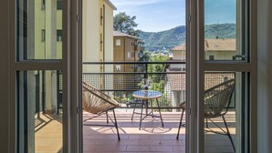 En balkon med fletstole og et lille bord, med udsigt over et boligområde med bygninger og bakker.