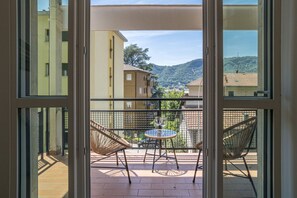 Ein Balkon mit Korbstühlen und einem kleinen Tisch, mit Blick auf eine Wohngegend mit Gebäuden und Hügeln.