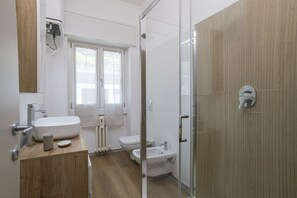 A modern bathroom with a wooden vanity, a glass shower enclosure, and a white toilet. - GuestHost - Cozy Apartment with Balcony (Como)