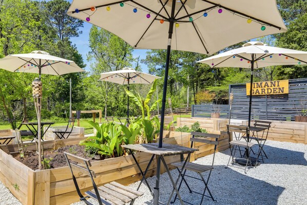 Un área de estar al aire libre con mesas y bancos de madera, rodeada de jardines elevados con plantas.