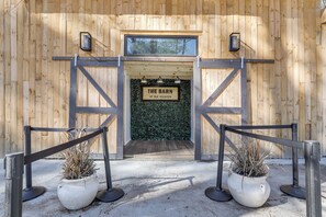 Ein hölzerner Barneingang mit einem Schild, das "The Barn at BLK Heaven" zeigt, und ein verschlossener Weg mit Blumentöpfen.