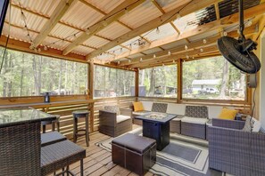 Un espacio de descanso al aire libre techado, con mobiliario de mimbre, una mesa y un ventilador.