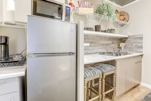 Eine moderne Küche mit einem Edelstahl-Kühlschrank, einer Kaffeemaschine und einem Holzbarhocker.