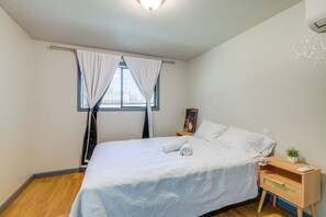 Ein Schlafzimmer mit einem Bett, einem Nachttisch, einem Fenster mit Vorhängen und einer Deckenleuchte.