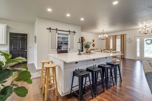 A modern kitchen with a central island, bar stools, and a dining area with a chandelier. - 8 Mi to Bentonville: Serene Retreat on 8 Acres (Pea Ridge)