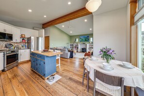 Une cuisine moderne avec un plancher en bois, un coin repas avec une table dressée pour deux personnes, et un salon avec un canapé et une cheminée.