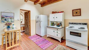 A kitchen with a wooden ceiling, a refrigerator, a stove, a cabinet, and a table with stools. - Traditional Taos Adobe Casita: Comfortable & Quiet (Taos)