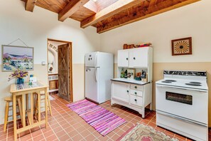 A kitchen with a wooden ceiling, a refrigerator, a stove, a cabinet, and a table with stools. - Traditional Taos Adobe Casita: Comfortable & Quiet (Taos)