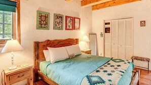 A bedroom with a wooden bed, two bedside tables, a window with a view, and a wardrobe. - Traditional Taos Adobe Casita: Comfortable & Quiet (Taos)