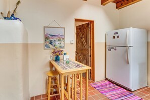 Una cocina con una mesa de madera, taburetes, un refrigerador, una puerta y piso de baldosas.