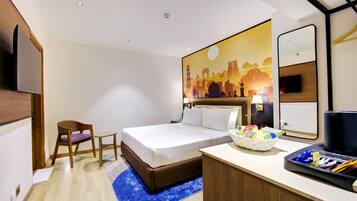 A hotel room with a bed, a chair, a desk with a basket, and a painting on the wall.