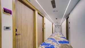 A hotel hallway with wooden doors, a carpeted floor, and a sign indicating room number 103. - Cozzet Yashobhoomi Dwarka (New Delhi)