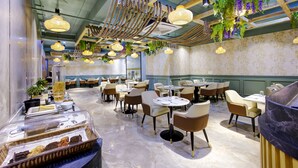 A restaurant with multiple tables and chairs, a buffet area with food items, and hanging plants. - Cozzet Yashobhoomi Dwarka (New Delhi)
