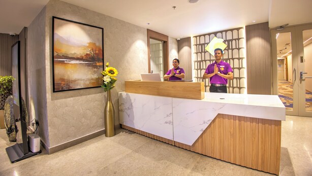 A reception desk with a marble top, a large landscape painting, and a vase with sunflowers. - Cozzet Yashobhoomi Dwarka (New Delhi)