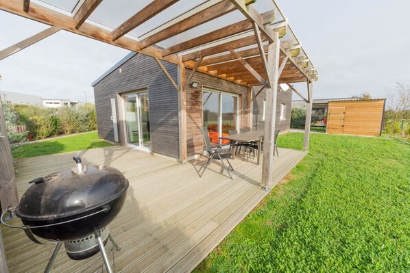 Un espace extérieur abrité comprenant un barbecue, une table avec des chaises et une terrasse en bois.