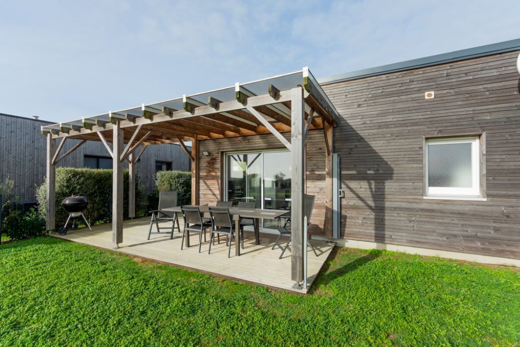 Un patio extérieur couvert, équipé d’une table et de chaises, d’un barbecue et d’une terrasse en bois.