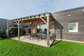 Un patio extérieur couvert, équipé d’une table et de chaises, d’un barbecue et d’une terrasse en bois.