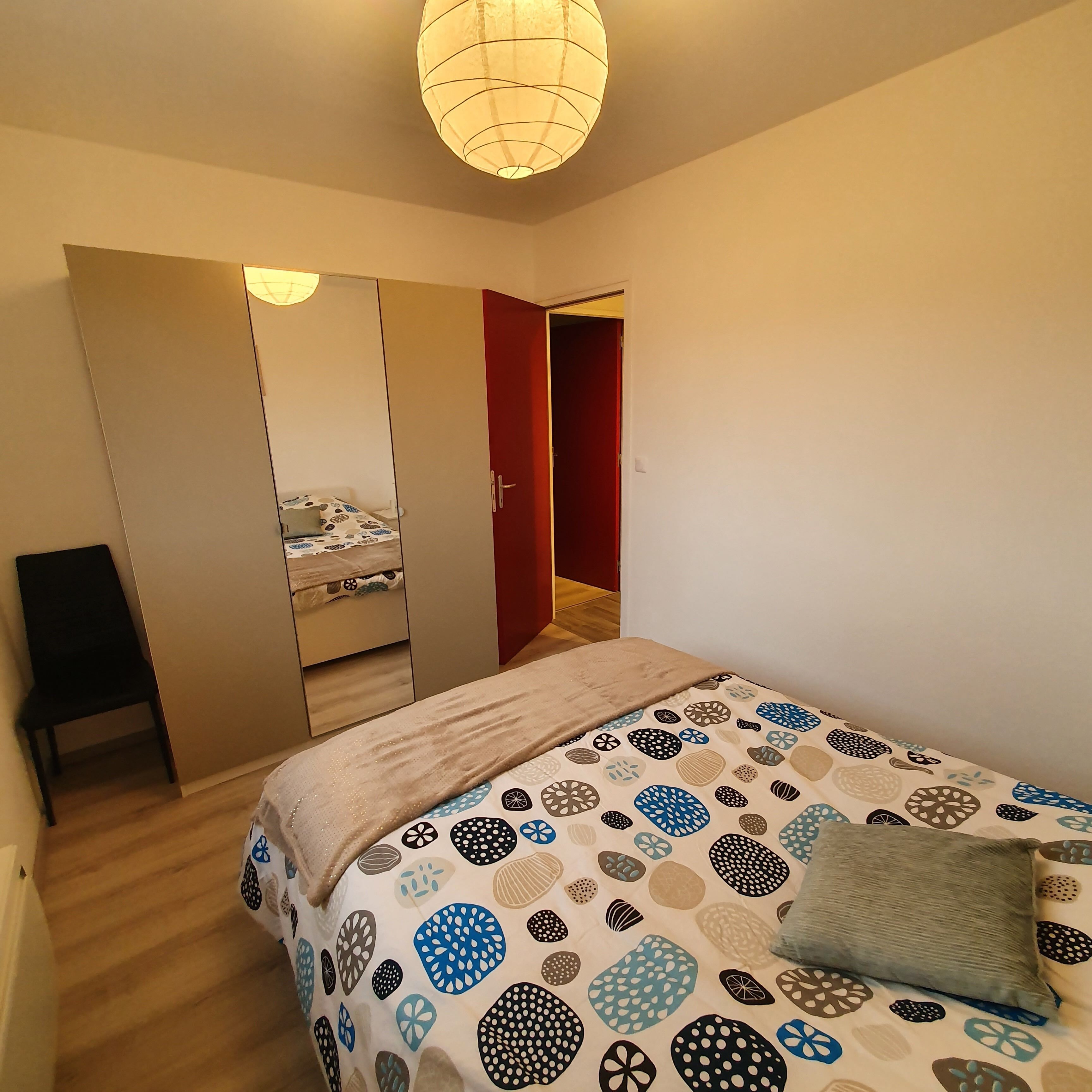 Ein Schlafzimmer mit Bett, Kleiderschrank, Spiegel und Tür.
