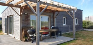 A wooden cabin with a covered patio, a barbecue grill, and outdoor seating. - LA MAISON DES DUNES, sleeps 7, near the sea (Les Moitiers-d'Allonne)