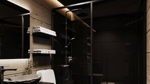 Ein modernes Badezimmer mit einer gläsernen Dusche, einer weißen Toilette und einem dunklen Waschtisch mit einer Beckenwaschanlage.
