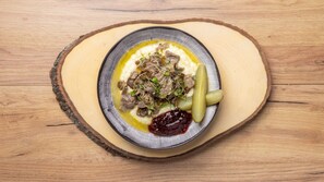 A plate of food with meat, pickles, and a creamy sauce on a wooden table. - Aurora Roof Window | 28m² Private Lux Arctic Cabin (Rovaniemi)