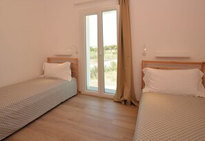 Ein Zimmer mit zwei Einzelbetten, einer Schiebeglastür nach draußen und einer Wandleuchte.