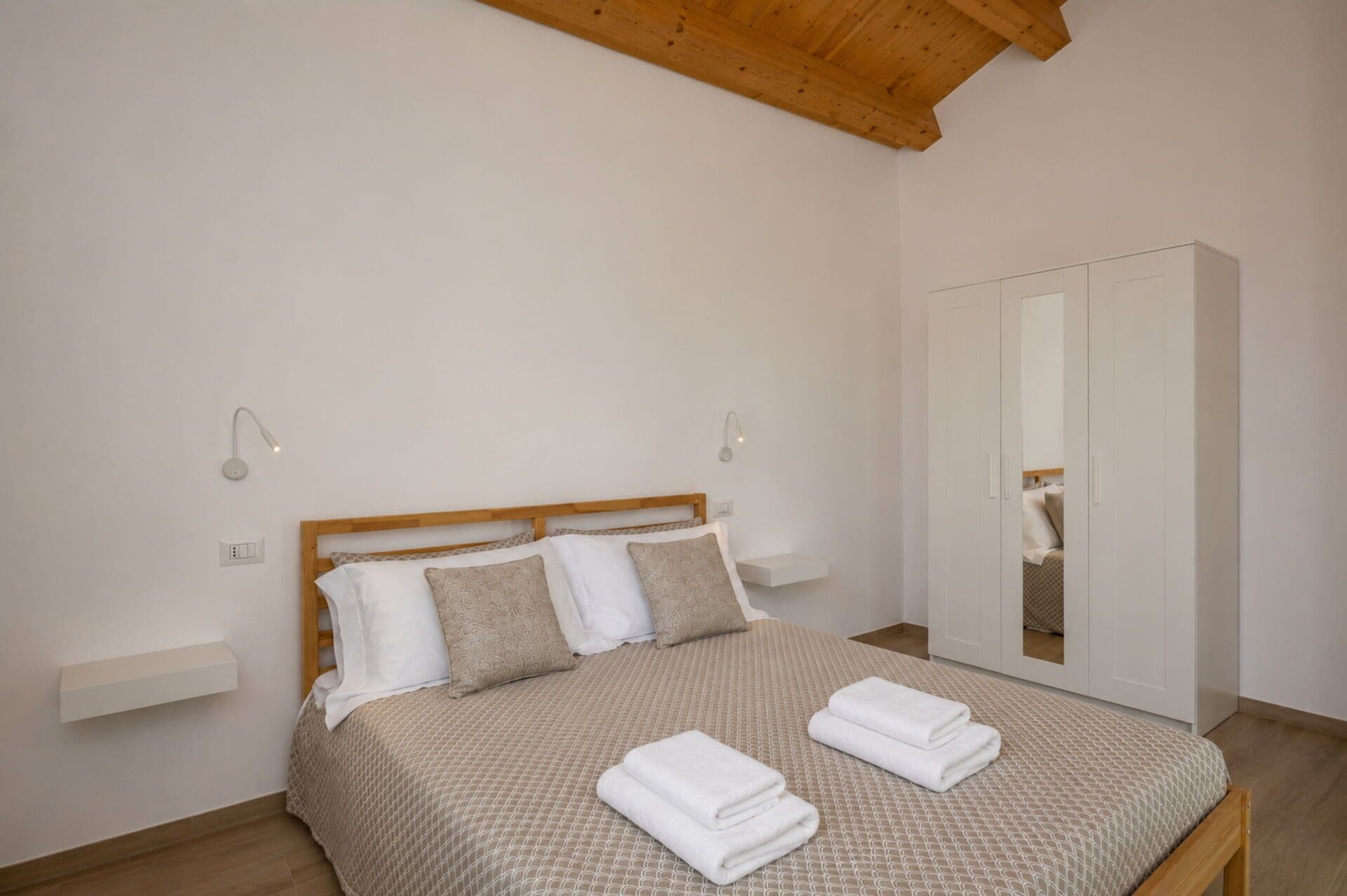 Ein Schlafzimmer mit einem Bett, zwei Nachttischen, einem Kleiderschrank und einer Decke mit Holzbalken.