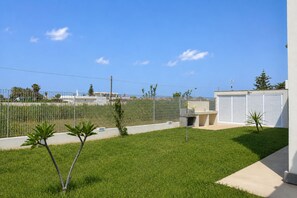 A fenced outdoor area with a grassy lawn, a small tree, and a building with a garage door. - Villa in Caucana with 2 bedrooms sleeps 4 (Caucana)