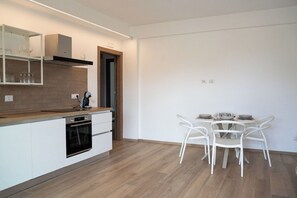 Una cocina moderna con armarios blancos, horno empotrado y comedor con mesa y sillas blancas.