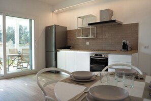 Una cocina moderna con refrigerador, horno y cafetera. Cuenta con un comedor con mesa y sillas.