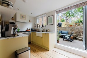 A kitchen with a central island, a dining area with a table and chairs, and a view of the outside through a sliding glass door. - Farmhouse Chic Studio Flat with Private Garden (Greater London)